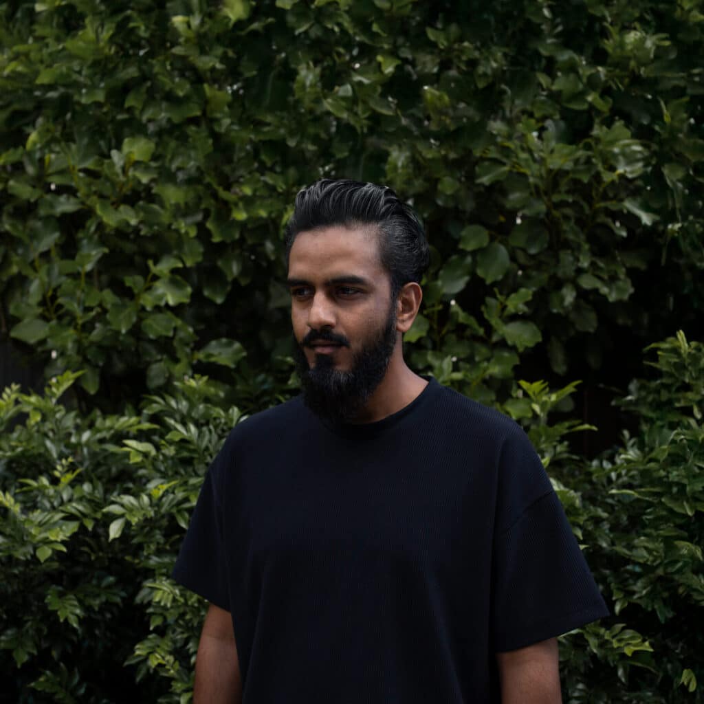 portrait of Mayank Thammalla standing in front of dense green leaves