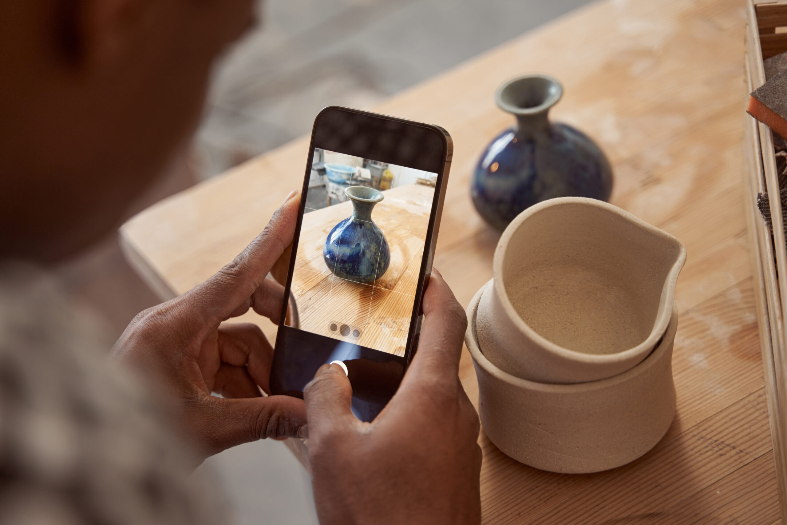ceramic artist using a phone to take photographs of their work for online selling.