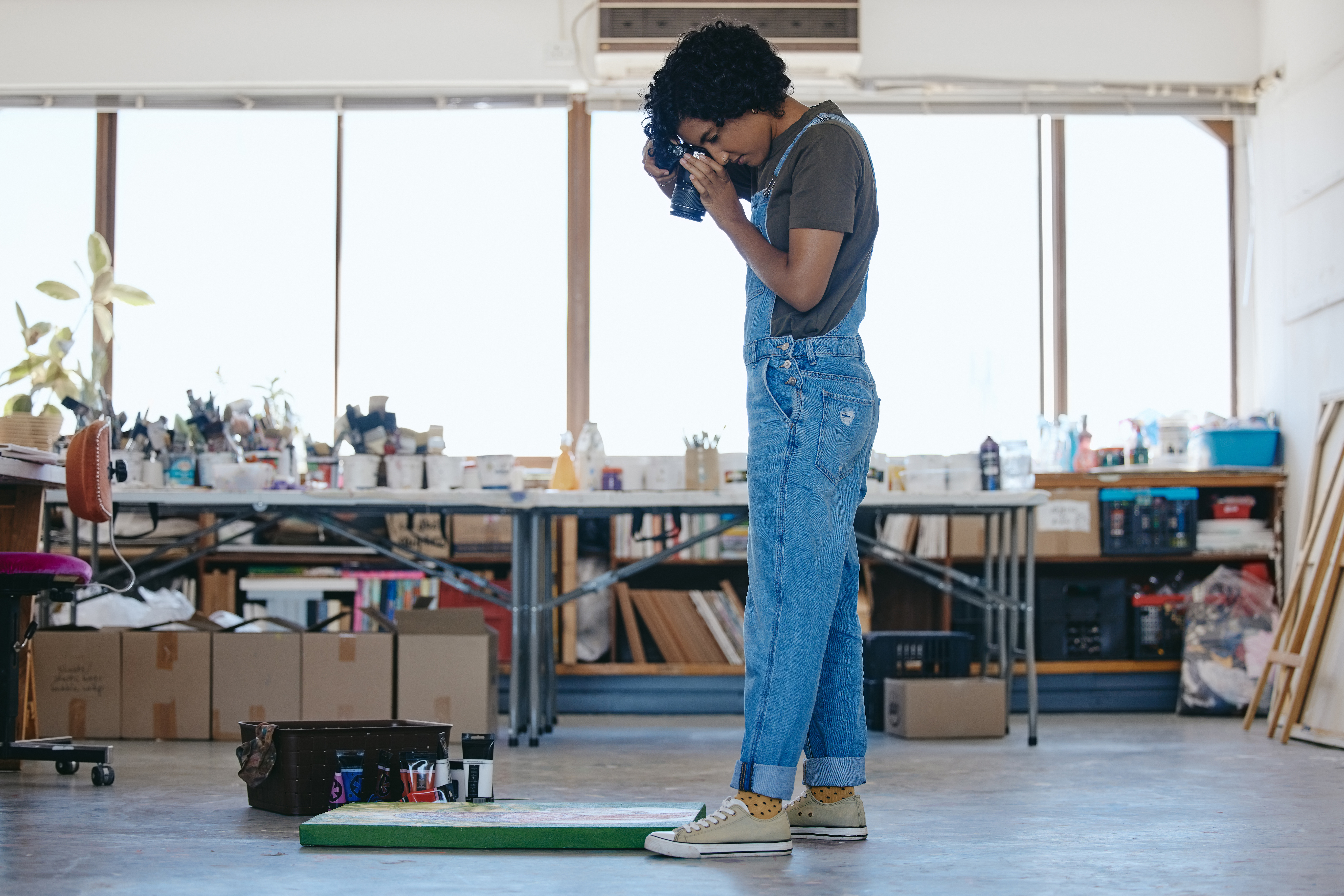 Creative woman artist in studio with camera, photographing art for exhibition and portfolio.