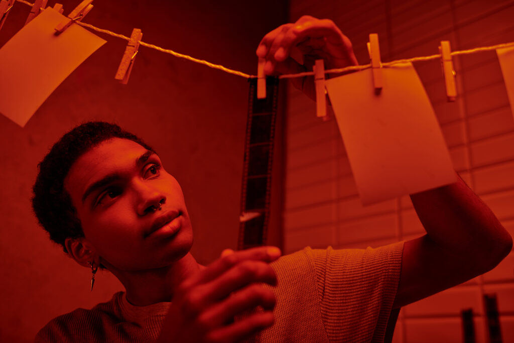 african american photographer hanging up developed film strip in a red lit darkroom
