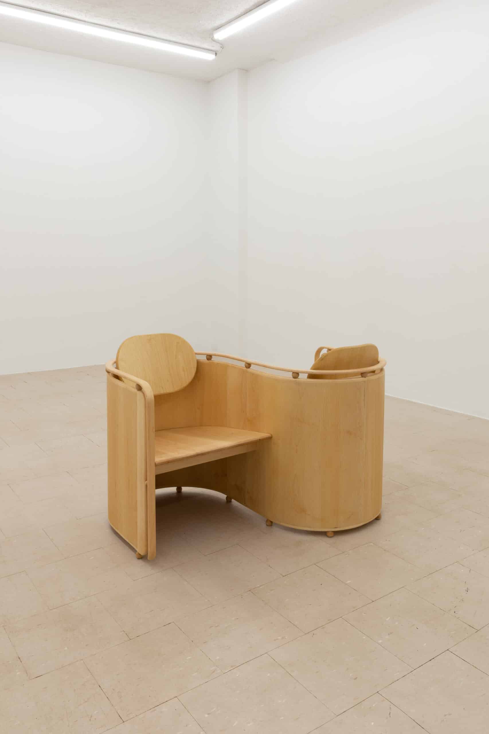 'S' shaped wooden chair with a seat in both curves of the shape, facing in opposite directions. Designed by artist Alison Postma "Kissing Chair"